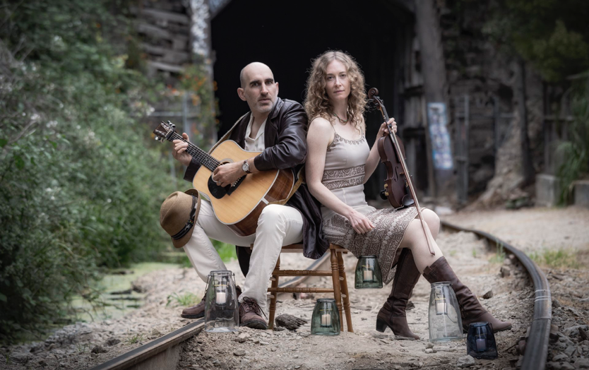 Musicians Dan Frechette & Laurel Thomsen posed on an old railway track with their instruments