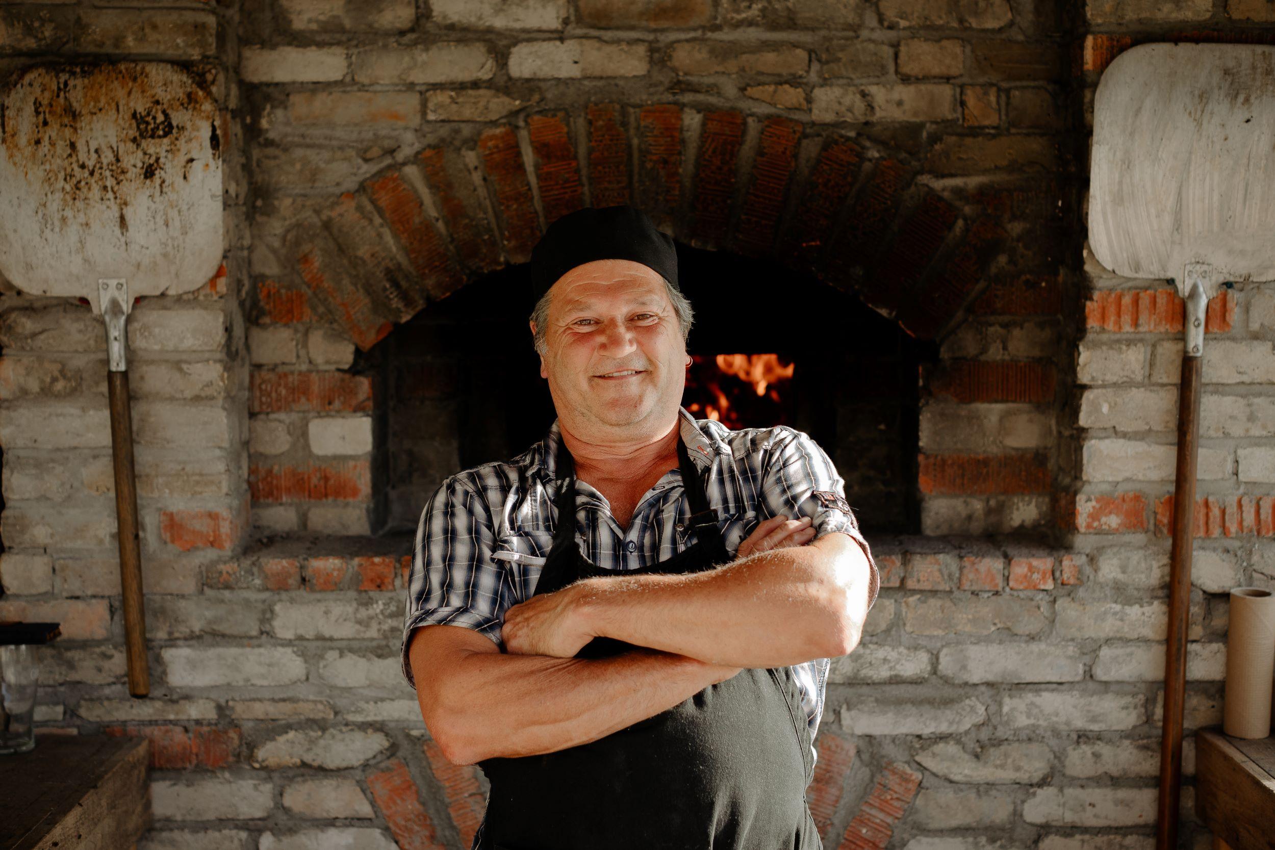 Michel standing in front of brick oven with arms crossed.