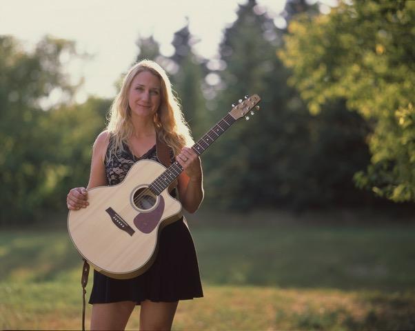 Ainsley Friesen holding her guitar with trees in the background.
